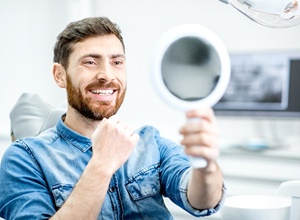 Man smiling in mirror, happy with investment in ceramic crown