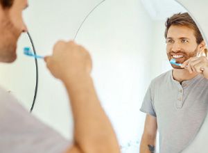 Handsome man brushing his teeth in front of bathroom mirror