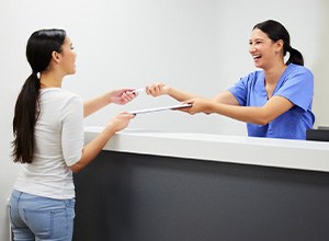 Young woman signing paperwork at dental office front desk
