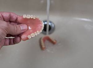 Person rinsing their dentures in the sink