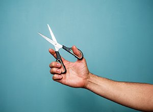 Man’s hand holding pair of scissors against teal background