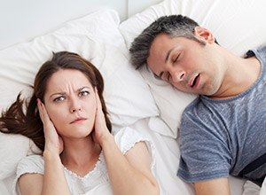 Woman covering ears next to snoring man