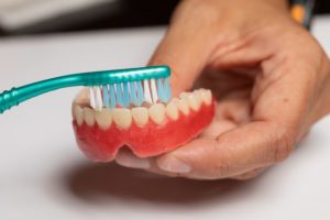 Using brush to gently remove denture stains in Abington