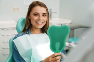 Satisfied patient holding hand mirror, admiring her veneers or crowns