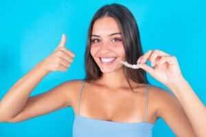 Woman holding Invisalign aligner and making thumbs up gesture 