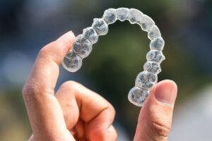 Hand holding Invisalign aligner between thumb and forefinger 